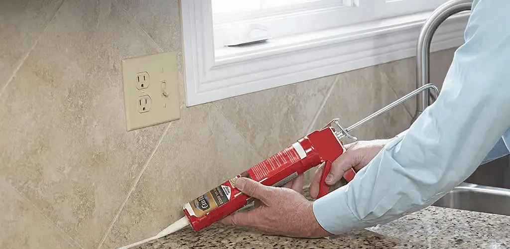 Handyman applying caulk along a kitchen backsplash and countertop seam in Chicago, IL